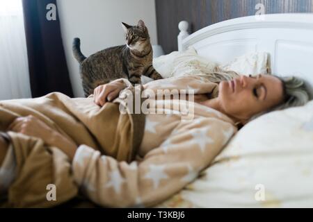 Cat controllando la donna addormentata su un letto. Il Pet sulla vostra camera da letto. Foto Stock