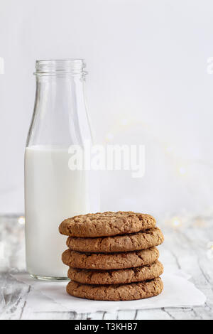 Pila di freschi fatti in casa biscotti di farina di avena con una bottiglia di latte su un tavolo bianco contro uno sfondo bianco. Foto Stock