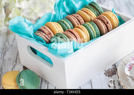 Assortimento di fresco francese macarons confezionato in un bel bianco scatola di legno con tessuto blu su bianco tavolo rustico.. Foto Stock