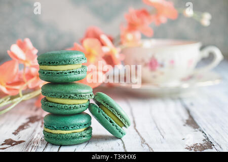 Pila di fresco francese il tè verde macarons su una bianca tavolo rustico con fiori e antichi tazza da tè sfocati in background.. Foto Stock