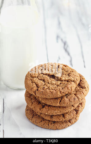 Scatto dall'alto della pila di freschi fatti in casa biscotti di farina di avena con una bottiglia di latte su un tavolo bianco contro uno sfondo bianco. Foto Stock