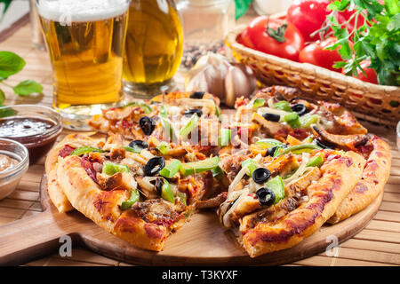 Pizza con pollo gyros, peperone verde, olive e cipolla sul tagliere. Servita con birra Foto Stock