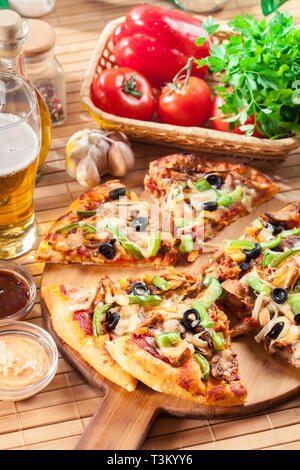 Pizza con pollo gyros, peperone verde, olive e cipolla sul tagliere. Servita con birra Foto Stock