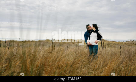 Incinta con il partner baciare e tenendo la pancia Foto Stock