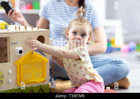 Simpatico Bimbo bimba gioca con busyboard. Bambini giocattoli educativi. Foto Stock