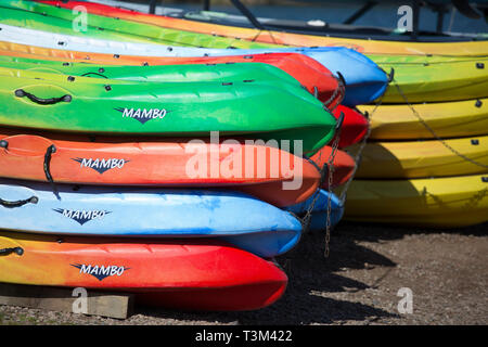 Vivacemente colorato canoe impilate in su e in attesa di essere utilizzati in una giornata di sole Foto Stock