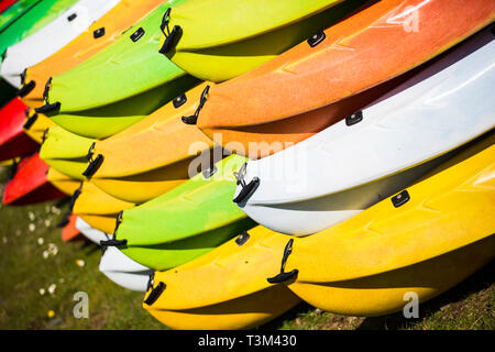 Vivacemente colorato canoe impilate in su e in attesa di essere utilizzati in una giornata di sole Foto Stock