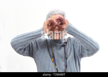 Senior donna guardando attraverso le dita come se si indossano occhiali su sfondo bianco Foto Stock