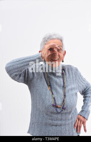 Senior donna guardando attraverso le dita come se si indossano occhiali su sfondo bianco Foto Stock