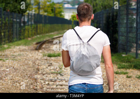 Giovane ragazzo bello camminare lungo la vecchia ferrovia, godendo i suoi dintorni sulla giornata di sole. Uomo di viaggiatori su ferrovia. Seguendo il vecchio percorso ferroviario. Foto Stock