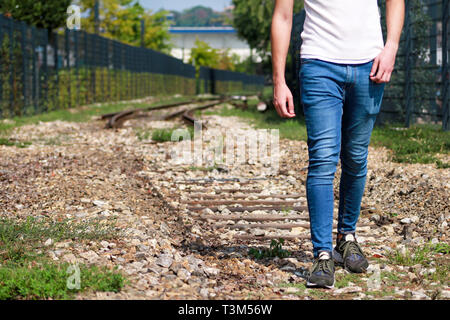 Giovane ragazzo bello camminare lungo la vecchia ferrovia, godendo i suoi dintorni sulla giornata di sole. Uomo di viaggiatori su ferrovia. Seguendo il vecchio percorso ferroviario. Foto Stock