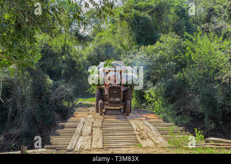 Colonia Independencia, Paraguay - June 20, 2018: Farmer with tractor in Paraguay drives over a winding wooden bridge. Foto Stock
