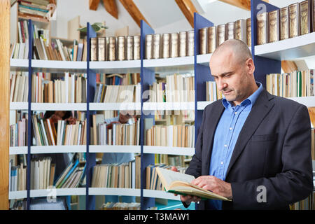 L'uomo come uno scienziato o un docente legge in un libro in una libreria Foto Stock