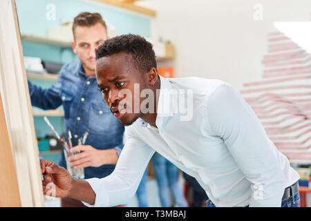 L'uomo africano come artista dipinge pitture su tela su cavalletto in studio Foto Stock