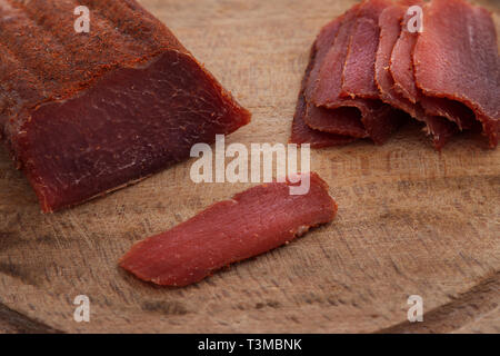 Basturma, essiccato filetto di carne di manzo tagliata a fette molto sottili, su di una superficie piana di legno, isolato su sfondo bianco. Foto Stock