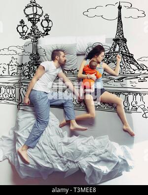 Parigi è chiamata. Vista superiore foto della giovane coppia e il loro bambino dorme in un grande letto bianco. Concetto di sogni. Dipinto di un sogno di viaggio in Francia, viaggio, avventure, vacanze in famiglia e di estate. Foto Stock