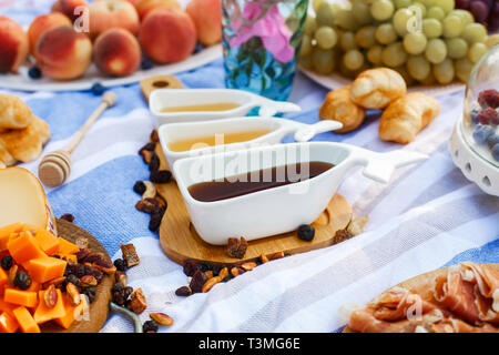 Set di tre sauceboats bianco con il dolce miele sul vassoio in legno a picnic food lay out dello sfondo. Foto Stock