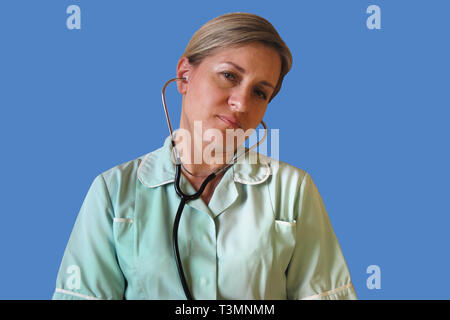 Un infermiere o un medico è pneumatici e esausto dopo laboriosi in ospedale o in clinica. Immagine isolata della donna bianca in uniforme di sedersi con uno stetoscopio in orecchie Foto Stock