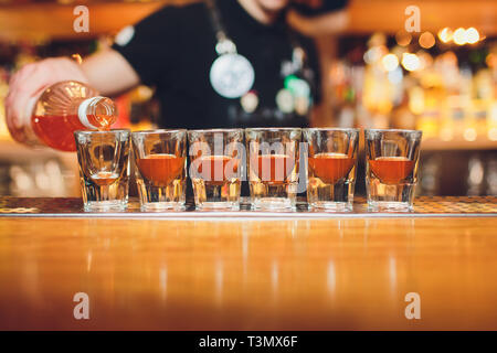 Barista versando forte bevanda alcolica in piccoli bicchieri sul bar, scatti Foto Stock