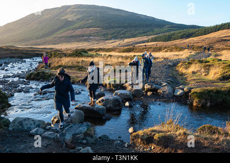 Turisti attraversando il fiume fragili sul modo per la Fata Piscine, Isola di Skye, regione delle Highlands, Scotland, Regno Unito Foto Stock