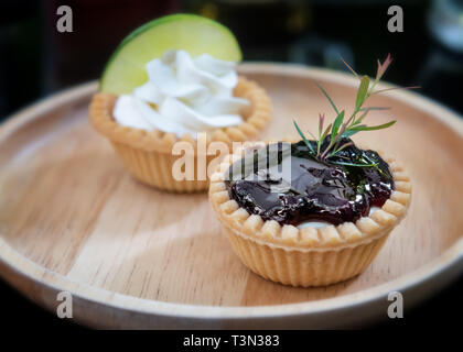 Mini frutta e torta di crema crostate nel piatto in legno con interni di bassa illuminazione. Foto Stock