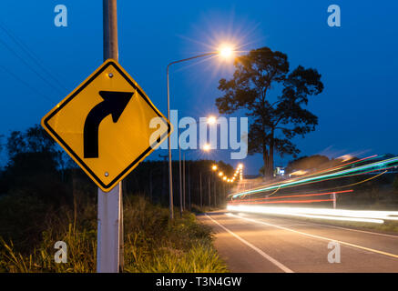 Girare a destra un cartello stradale con auto linea paglierino motion in twilight sky time. Foto Stock