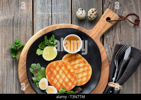 Grigliata di fettine rotonde di formaggio greco con miele, insalata verde e uovo di quaglia. Appartamento giaceva su tavola in legno rustico. Foto Stock