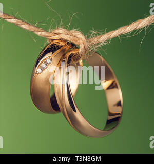 Due anelli di nozze legato con una corda su uno sfondo verde, primo piano Foto Stock