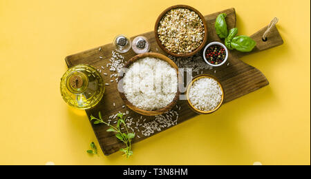 Banner di diversi tipi di riso su una tavola di legno realizzata in legno d'ulivo. Sfondo di cibo con le foglie di basilico e olio di oliva. una sana cucina casalinga Foto Stock