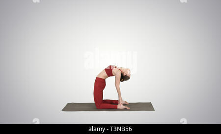 Sporty bella giovane donna a praticare yoga, facendo Ushtrasana, Camel pongono sul gradiente dello sfondo. Foto Stock