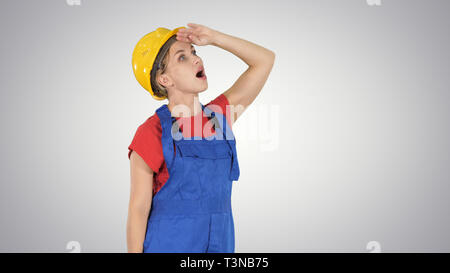 Ingegnere lavoratore edile donna che guarda verso l'alto stupiti sul gradiente dello sfondo. Foto Stock