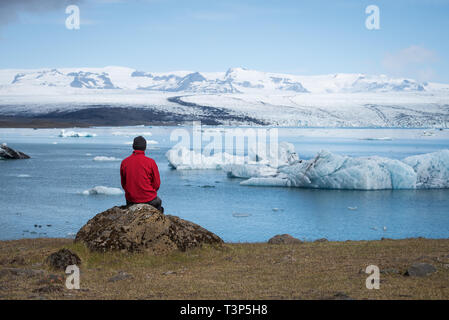 L'uomo traveler in giacca rossa si trova sulle sponde di un lago. Paesaggio estivo con laguna glaciale, di ghiacciai, iceberg nel sud-est dell' Islanda, Europa Foto Stock