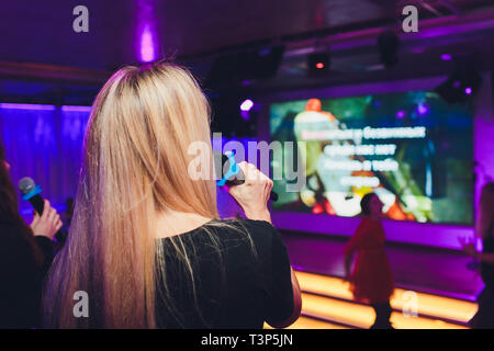 Felice bionda cantando il karaoke in mic in un bar Foto Stock