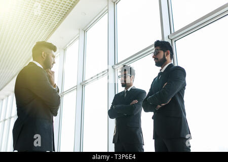 Sagome di tre asiatici corporate executives in piedi di fronte a finestre discutere di affari . Foto Stock