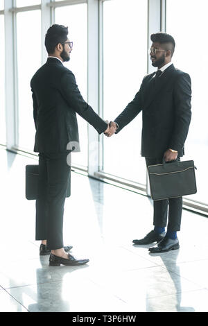 Lunghezza piena vista laterale di uomini di affari si stringono la mano in ufficio Foto Stock