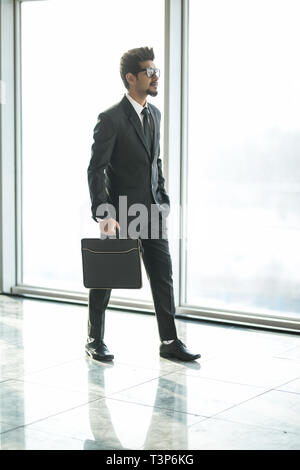Commerciante indiano a piedi in ufficio interno con grandi finestre con vista sul centro business Foto Stock