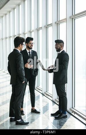 Sagome di tre asiatici corporate executives in piedi di fronte a finestre discutere di affari con computer portatile. Foto Stock