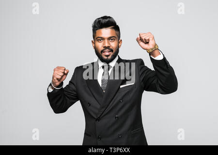 Gioiosa giovane imprenditore indiano per celebrare il successo. Emozionato indiana di abbigliamento casual alzando i pugni nel gesto vincente e gridando. Foto Stock