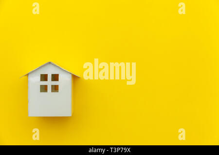 Semplicemente dal design minimale con bianco in miniatura toy casa isolata su giallo colorato moderno e alla moda fashion background. Ipoteca assicurazione immobiliare sogno
