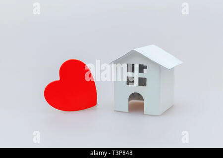 Semplicemente dal design minimale con bianco in miniatura toy house e cuore rosso isolato su sfondo bianco. Ipoteca di proprietà di assicurazione casa da sogno concetto. Copia