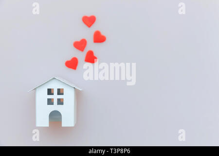 Semplicemente dal design minimale con bianco in miniatura toy house e cuore rosso isolato su sfondo bianco. Ipoteca di proprietà di assicurazione casa da sogno concetto. Appartamento Foto Stock