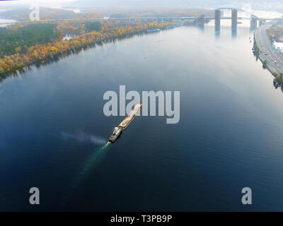 Scenic aerial cityscape di Kiev e il fiume Dnipro al tramonto. Rimorchiatore chiatta di supporto con sabbia di materiali alla rinfusa voce lungo il fiume Dnieper. Ucraino Foto Stock