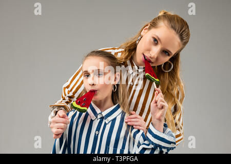 Piacevole soddisfatto buona-cercando ragazze in costumi luminosi mangiando caramelle Foto Stock