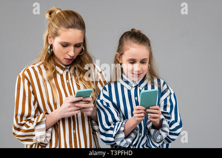 Focalizzato belle dame in camicie a righe controllando attentamente i social media Foto Stock