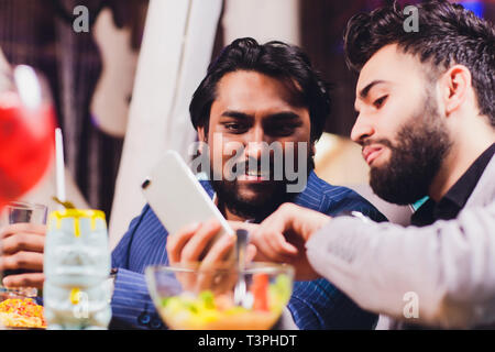 Due Uomo nel Bar tenere bicchieri sedersi al bancone e bere cocktail, Allegro amici Meeting Bar Comunicare Parlare. Foto Stock