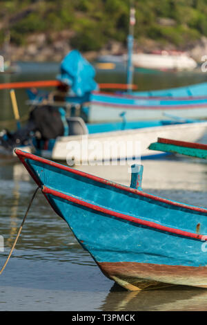 Tradizionale in legno aperto long tail o longtail barche da pesca ormeggiate in una tranquilla baia sulla spiaggia a Ko Phangan, Thailandia. Foto Stock