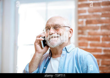 Allegro senior nonno parlando con il telefono vicino alla finestra a casa Foto Stock