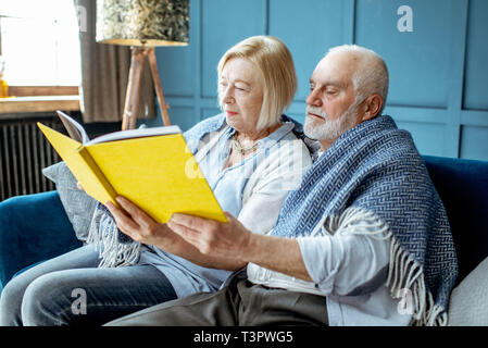 Bella coppia senior libro seduti avvolto con caldi plaid sul divano di casa Foto Stock