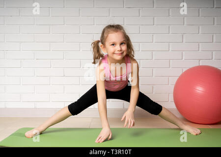 Allegro bambina facendo sport esercizi sul tappetino a casa, bambini sport e yoga. Foto Stock