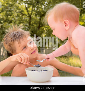 Concetto di nutrizione. Cibo sano. Alimenti biologici. La nutrizione per i bambini. Degustazione di bambini mirtillo seduti in giardino in estate giornata di sole. Carino boy Foto Stock